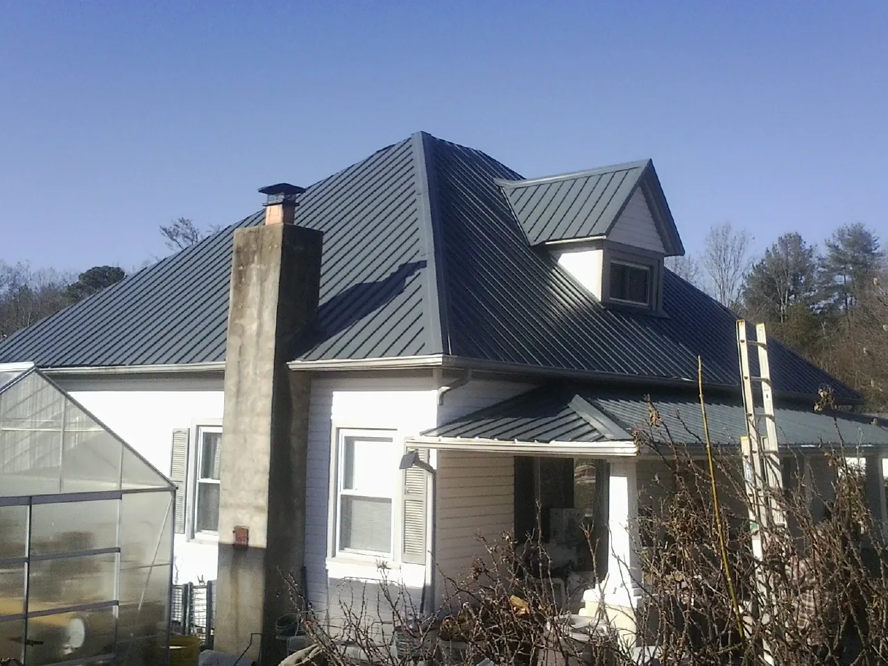 Dark blue standing seam metal roof on a white farmhouse with dormer — Slate & Tile Roof Repair by Roofing Brothers in Wakefield