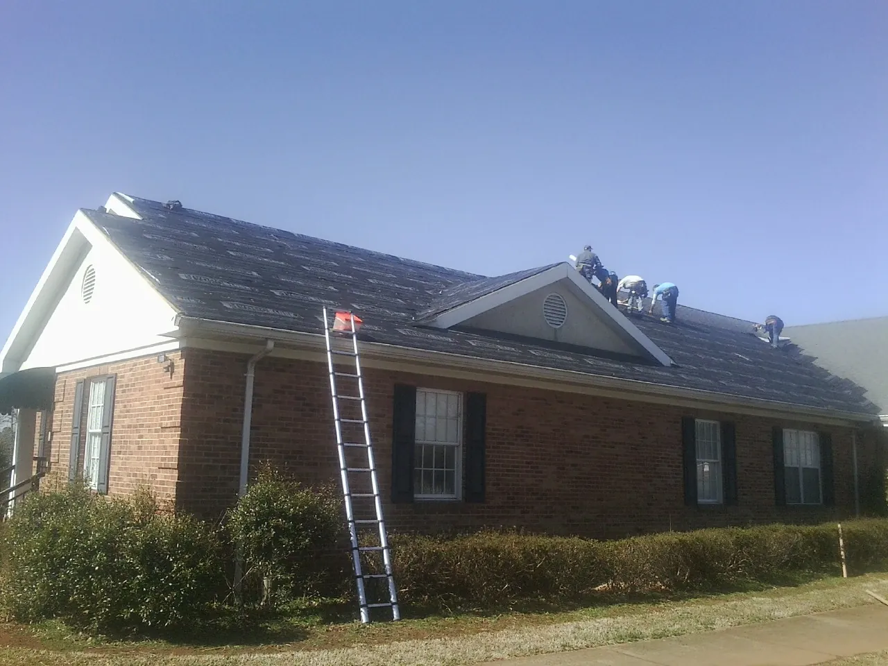 Crew tearing shingles off a brick ranch roof with a ladder set — Metal Roof Repair work by our crew in Wakefield